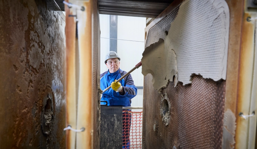 An employee in protective clothing using a spatula to remove filter cake from a filter plate in a chamber filter press.