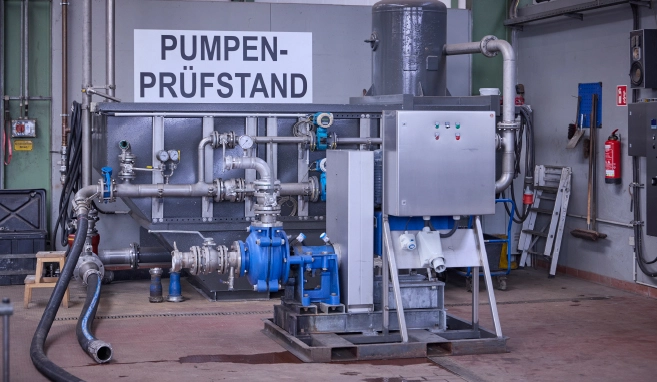 A pump test stand with pipe, valves and measuring instruments in an industrial building.