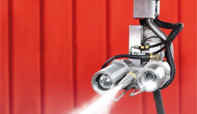 An industrial high-pressure nozzle and hose system spraying water in front of a red background.