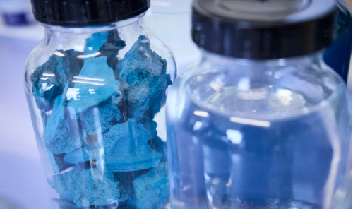 Glass jars containing blocks of blue material and a clear liquid in a laboratory environment, A close-up image focusing on the structure of the substances.