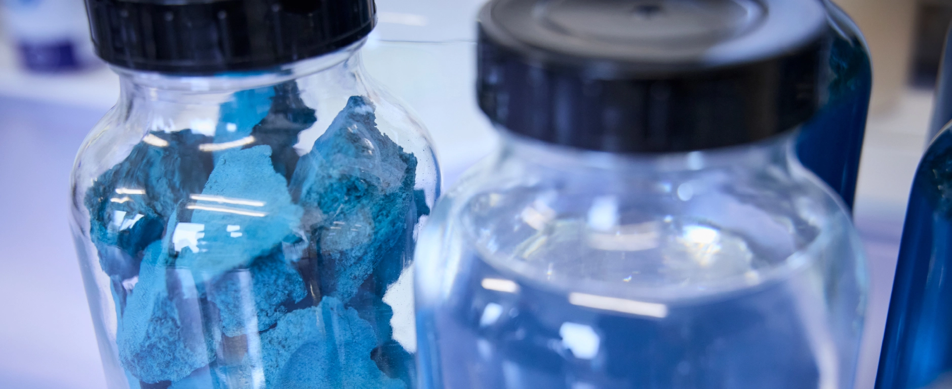 Glass jars containing blocks of blue material and a clear liquid in a laboratory environment, A close-up image focusing on the structure of the substances.