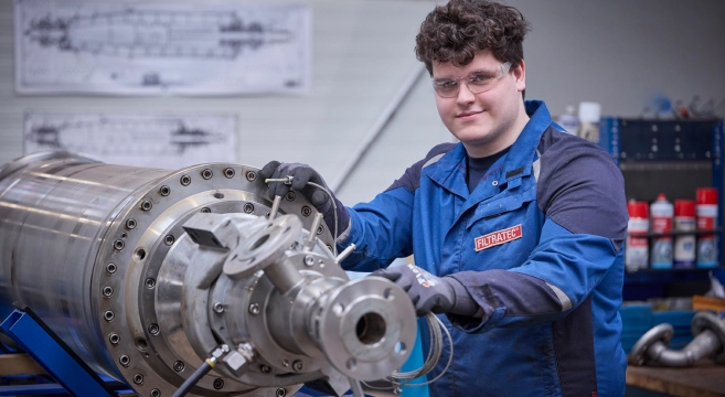 A FILTRATEC employee or apprentice wearing protective clothing working on an industrial filter part in a workshop environment.