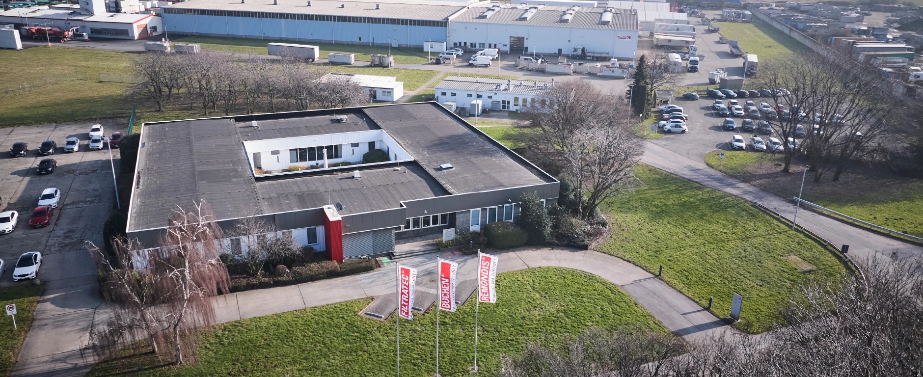 An aerial view of a business premises with an office building, production plants and FILTRATEC, BUCHEN and REMONDIS flags.