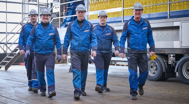 Five employees wearing FILTRATEC protective clothing and hard hats walking together through an industrial building in front of a filter press