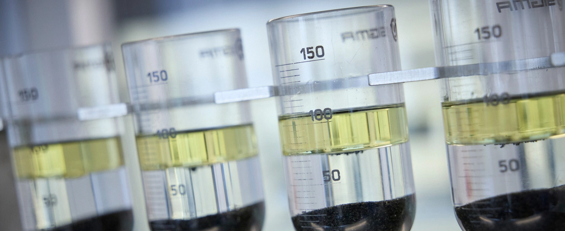Beakers containing a two-phase liquid and dark sediment in a laboratory environment.