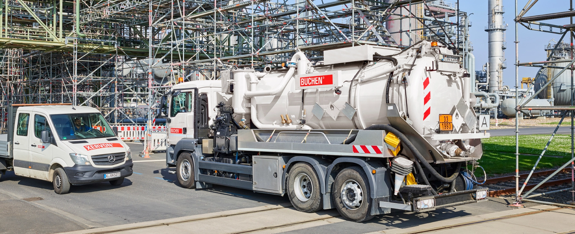 An industrial plant with pipes and scaffolding, in the foreground a BUCHEN vacuum truck and a service vehicle on the business premises.