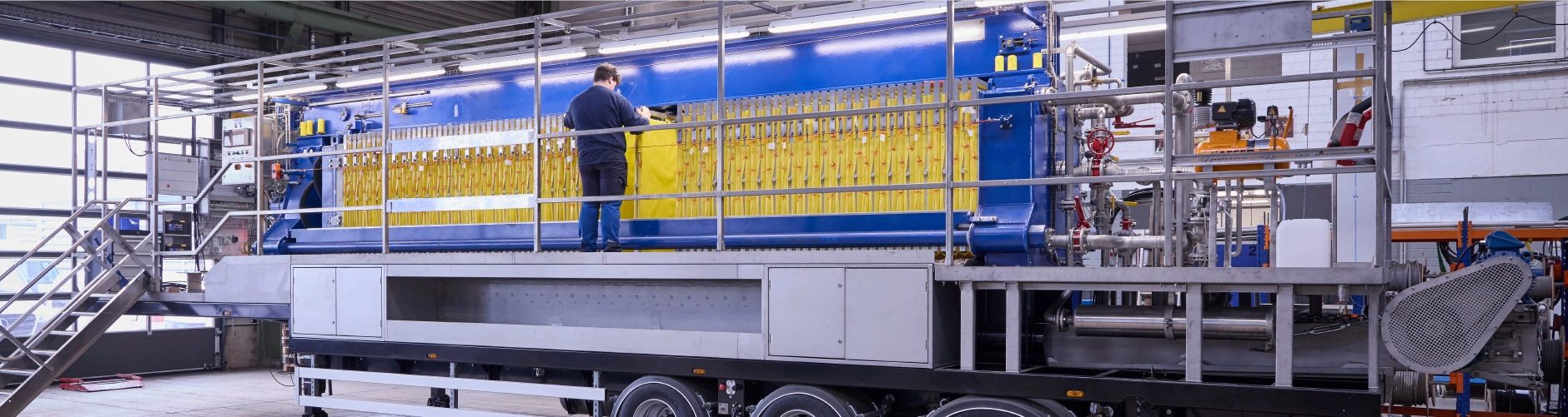 A new mobile press in an industrial building, an employee standing on a platform checking the filter plates.
