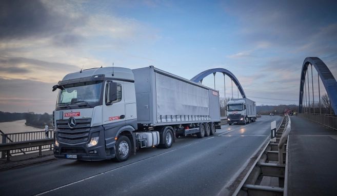 Two FILTRATEC lorries driving over a bridge at dusk, a river landscape and other lorries in the background.